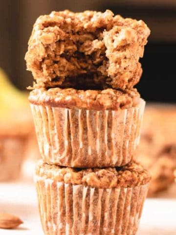 almond banana muffins stacked with a bite out of the top one.