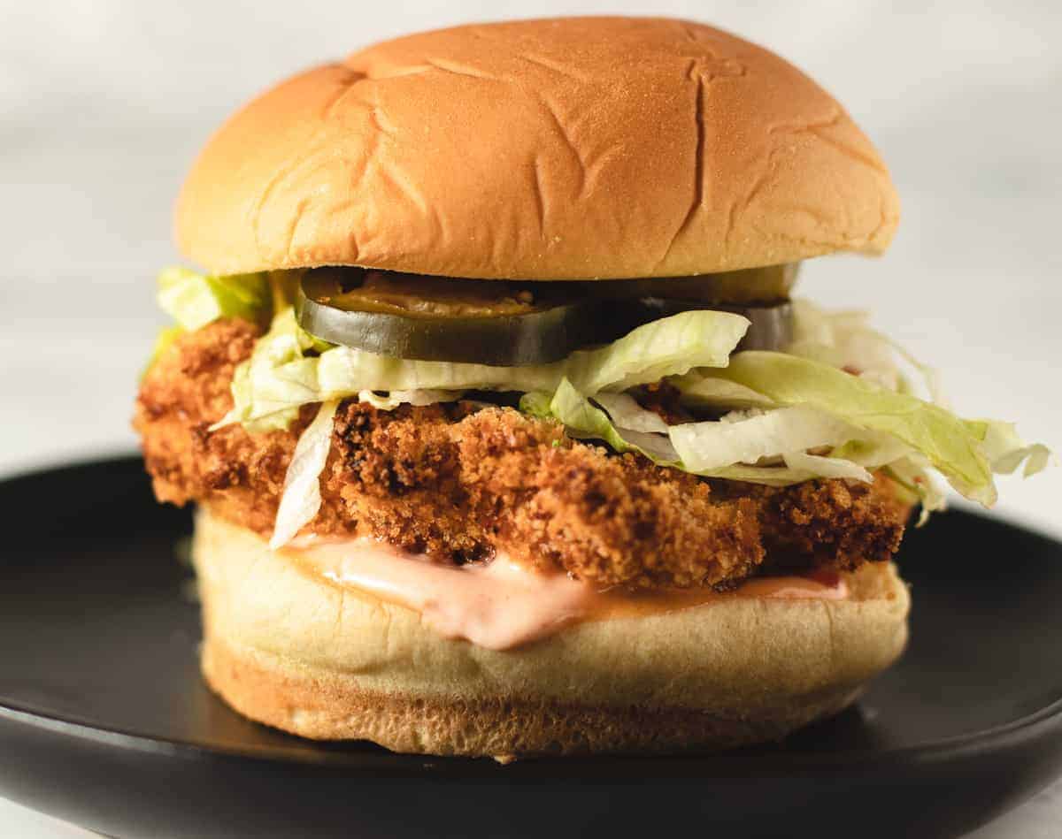 Air Fryer Chicken sandwich with sauce and lettuce sitting on a black plate. 