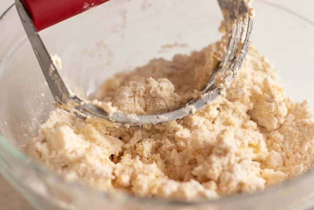 a dough blender in a bowl of the flour, salt, egg and sour cream. The dough blender is used to  mix in the butter