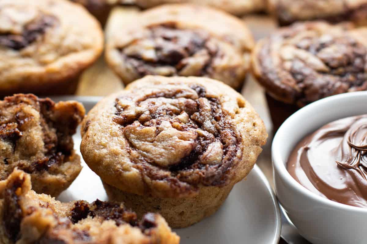 Banana Nutella muffins baked sitting on white plate with a small bowl of nutella sitting on the right. 