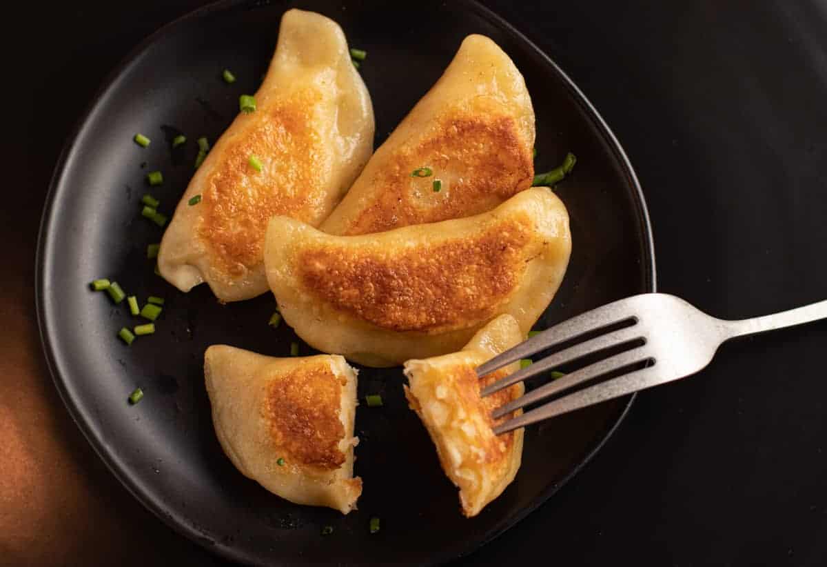 4 finished seared pierogi on a black plate with chive garnish