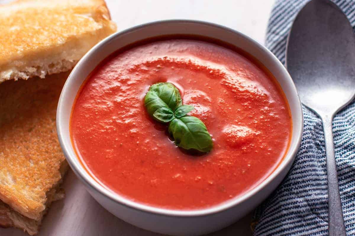 roasted tomato soup in a white bowl with grilled cheese sandwich