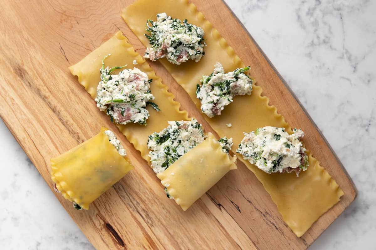 Three lasagna noodles with 3 tablespoons of the filling on boiled noodles. First noodle is shown as rolled.