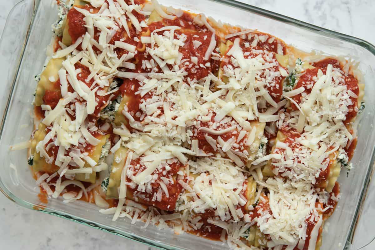 Lasagna rolls in a glass 9 by 13 dish finished with cheese on top ready to be baked in oven.