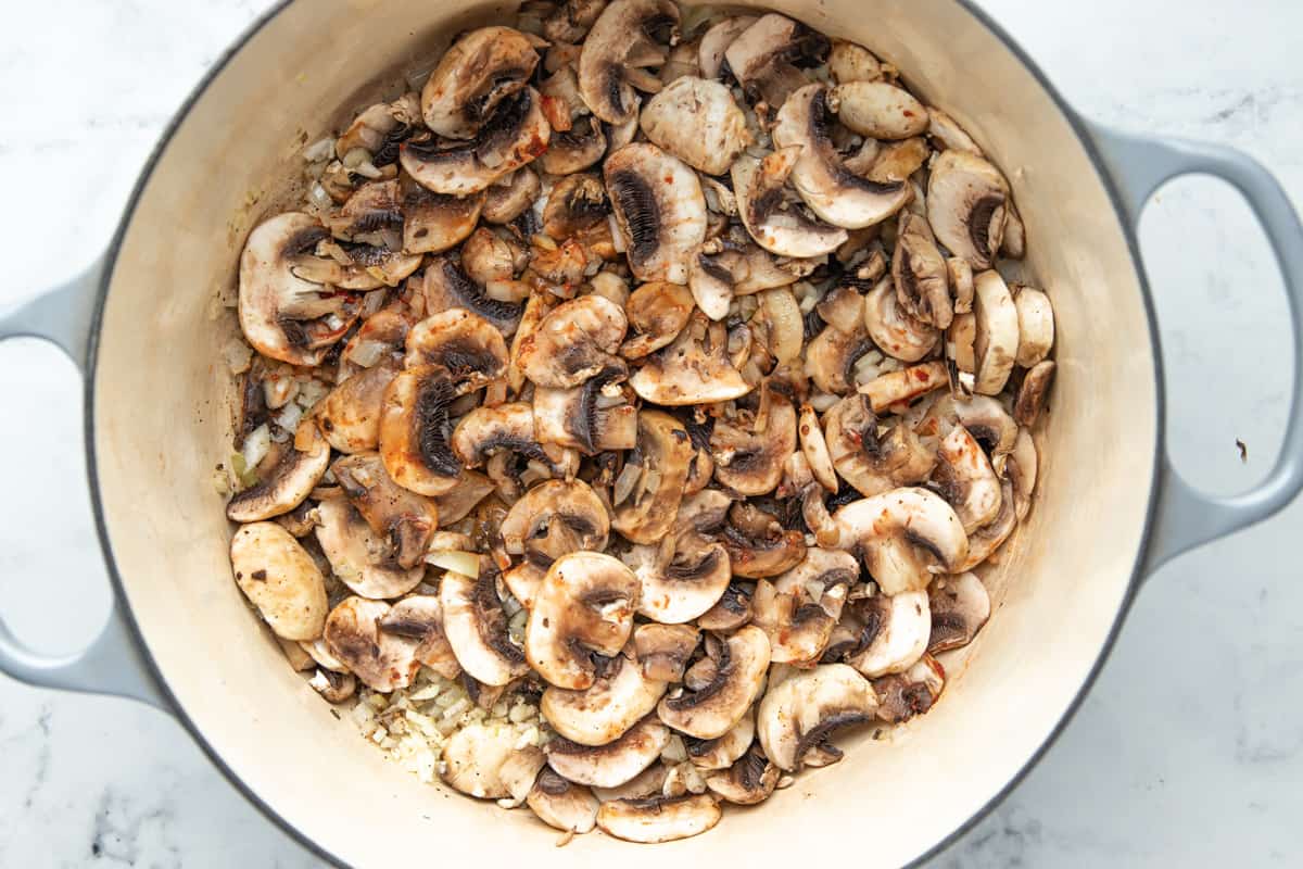 Sliced mushrooms with onion, onion garlic, tomato paste, salt, and pepper in a dutch oven