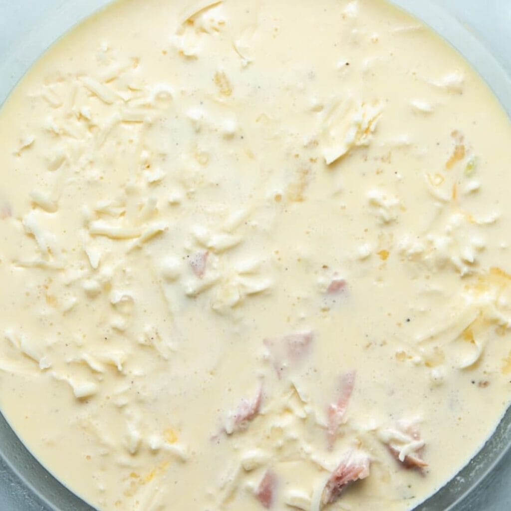 Pouring the egg and cream custard over ham, leeks, and Gruyère in the pie dish.
