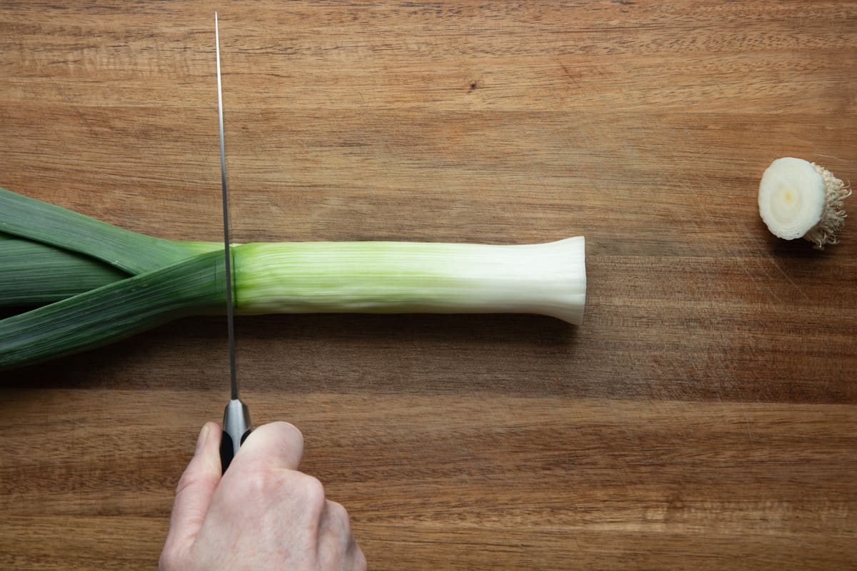 leek on cutting board with knife set to cut off the top dark green top of leek