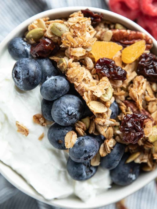 white bowl of yogurt with blueberries and granola on top