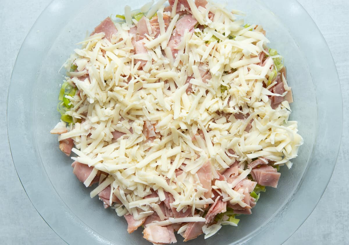 A greased pie plate with leeks, ham and cheese 