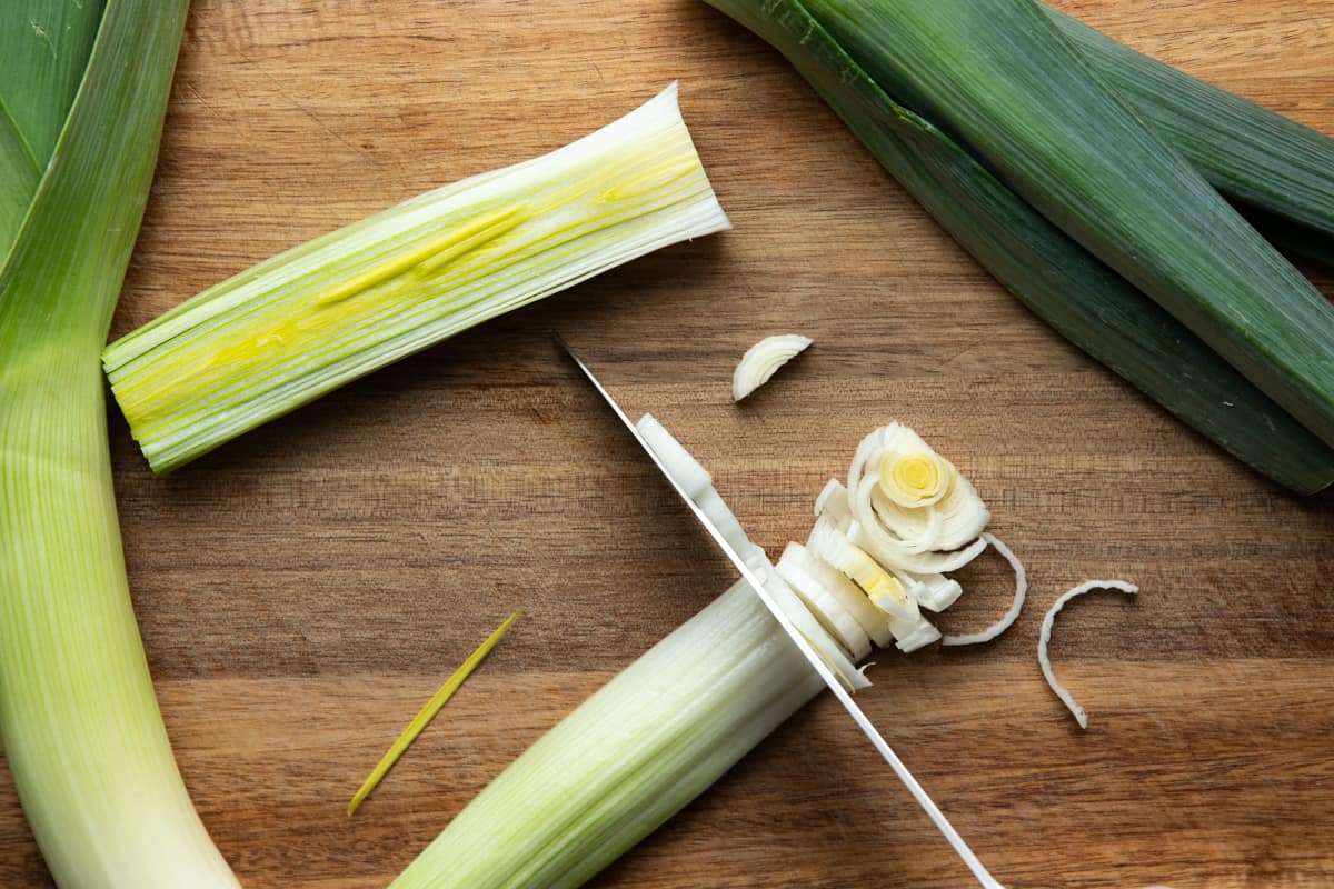 leek on cutting board shown cut in half and being sliced into half-moon slices