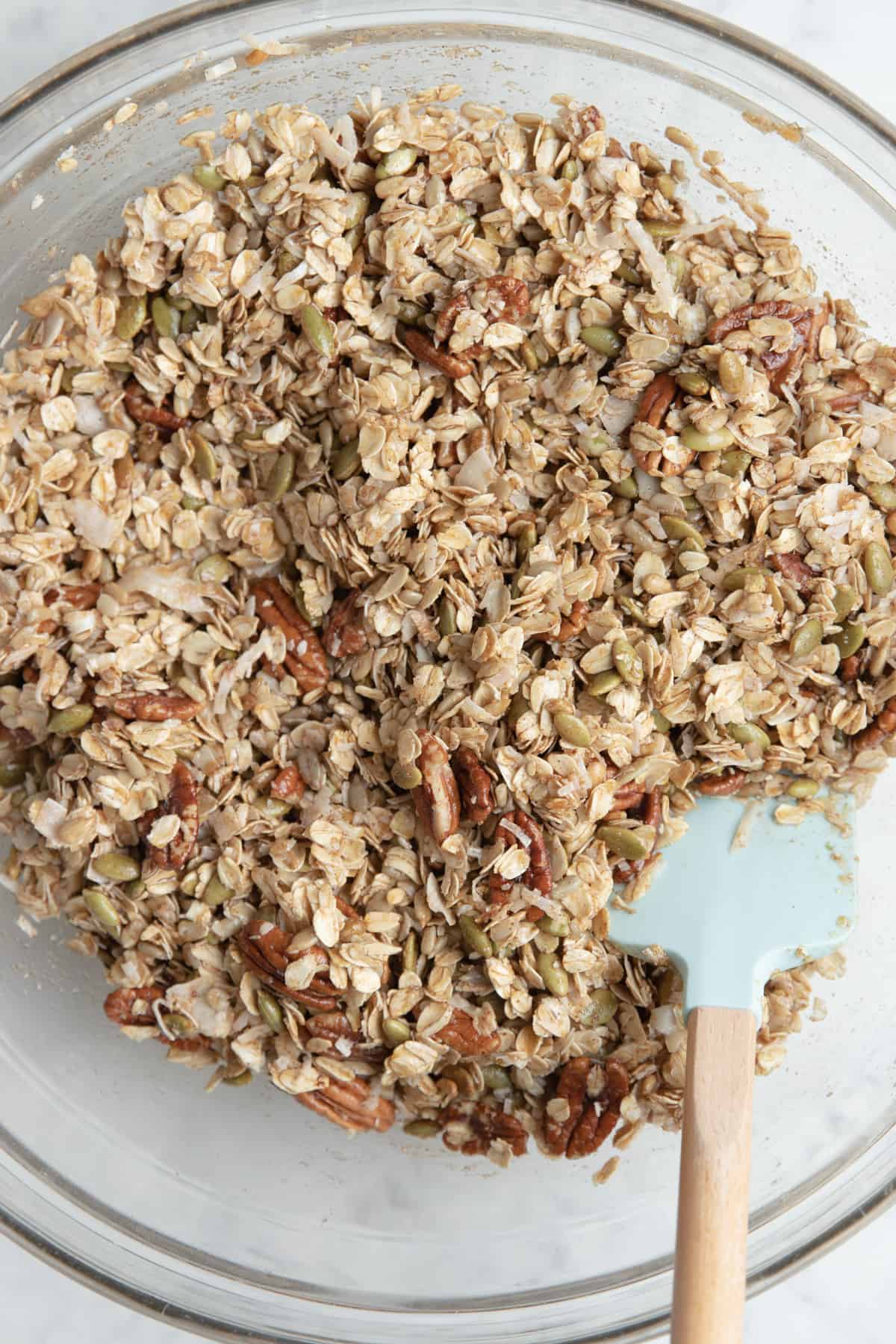 clear bowl with granola ingredients with a spatula to mix them together