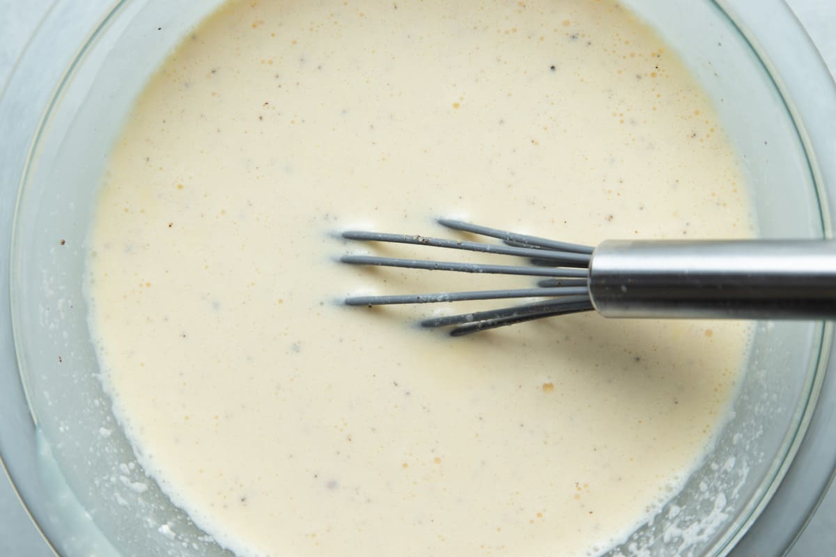 A clear bowl with the mixture of eggs, cream, slurry, milk and seasonings