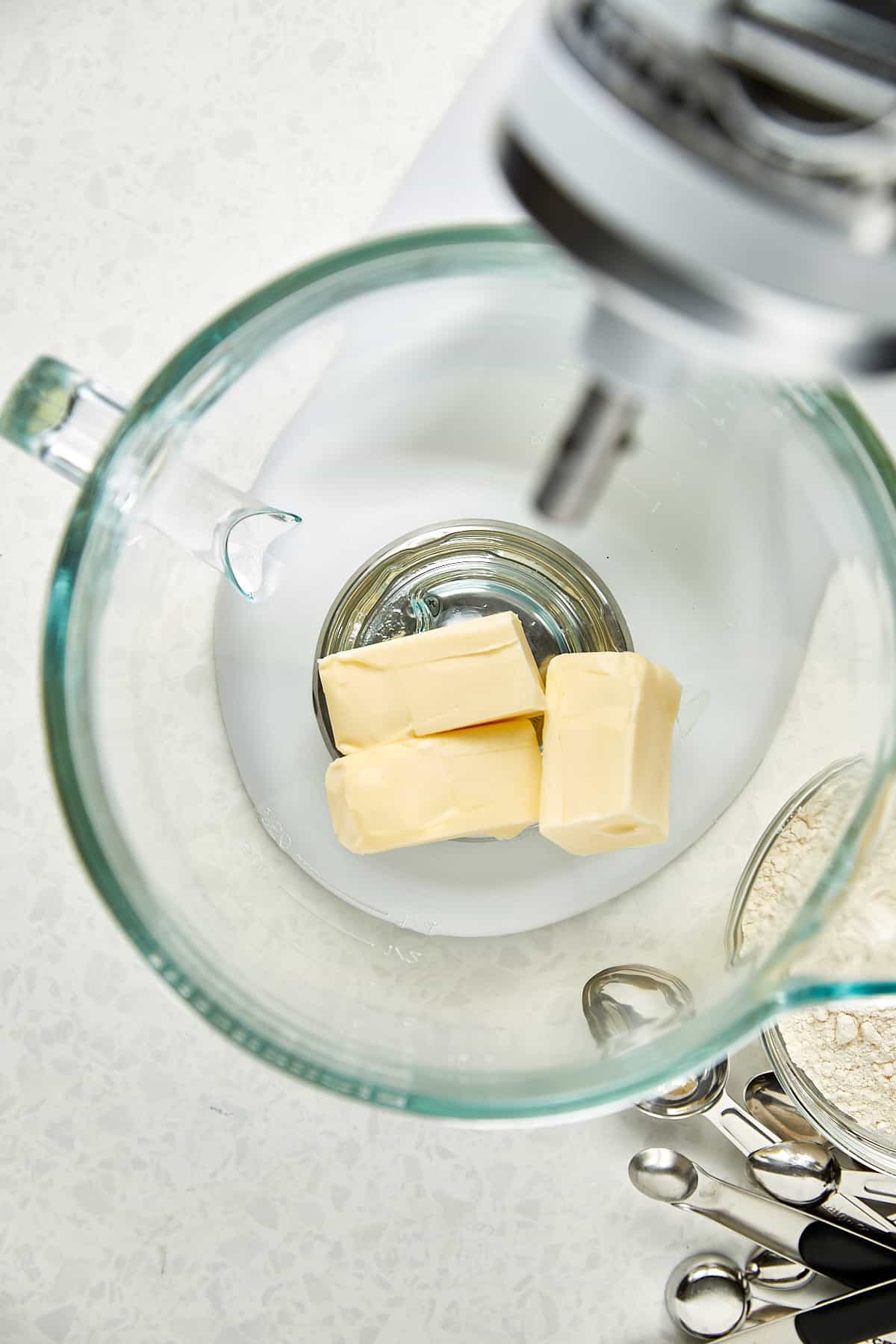 unsalted butter in clear mixer bowl sitting on a kitchen aid mixer.