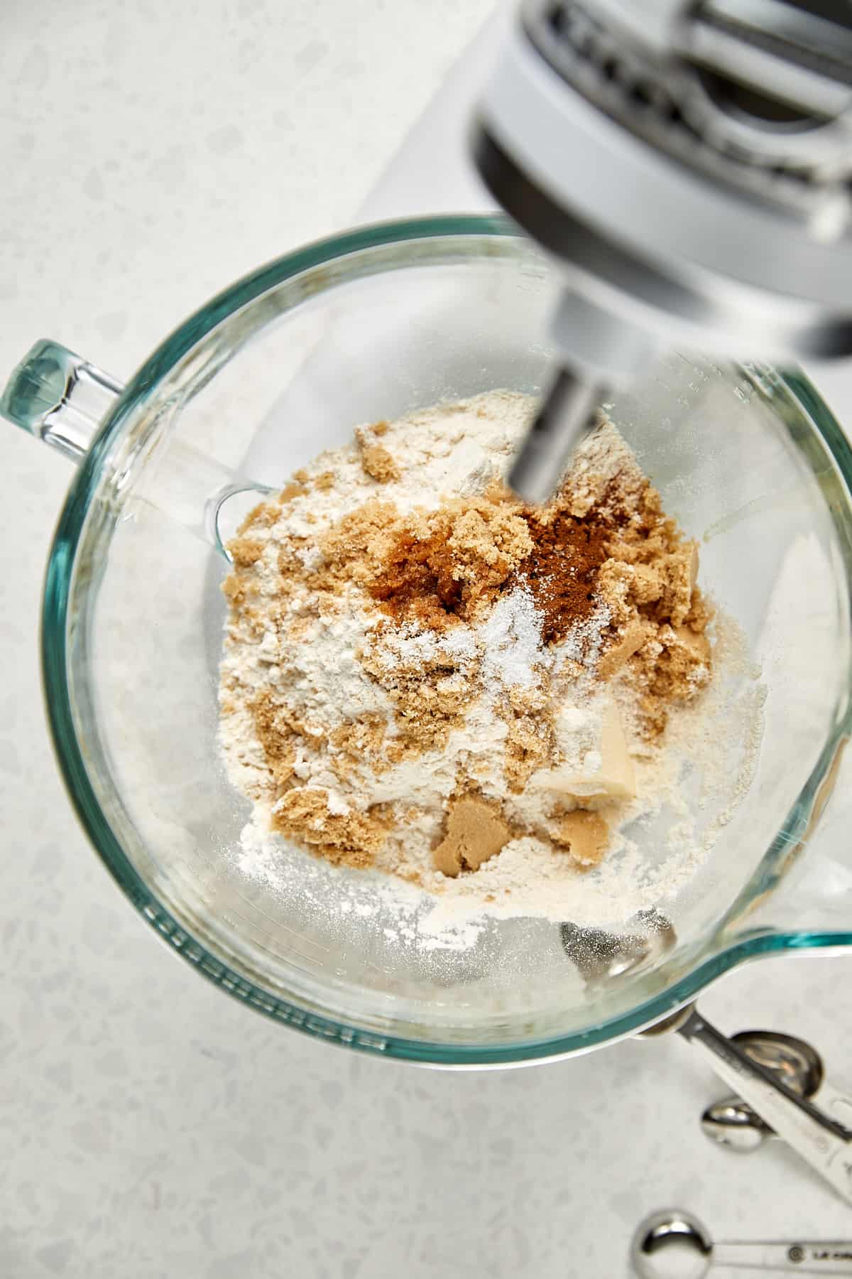 clear mixer bowl with flour, brown sugar, cinnamon and kosher salt sitting on a kitchen aid mixer.