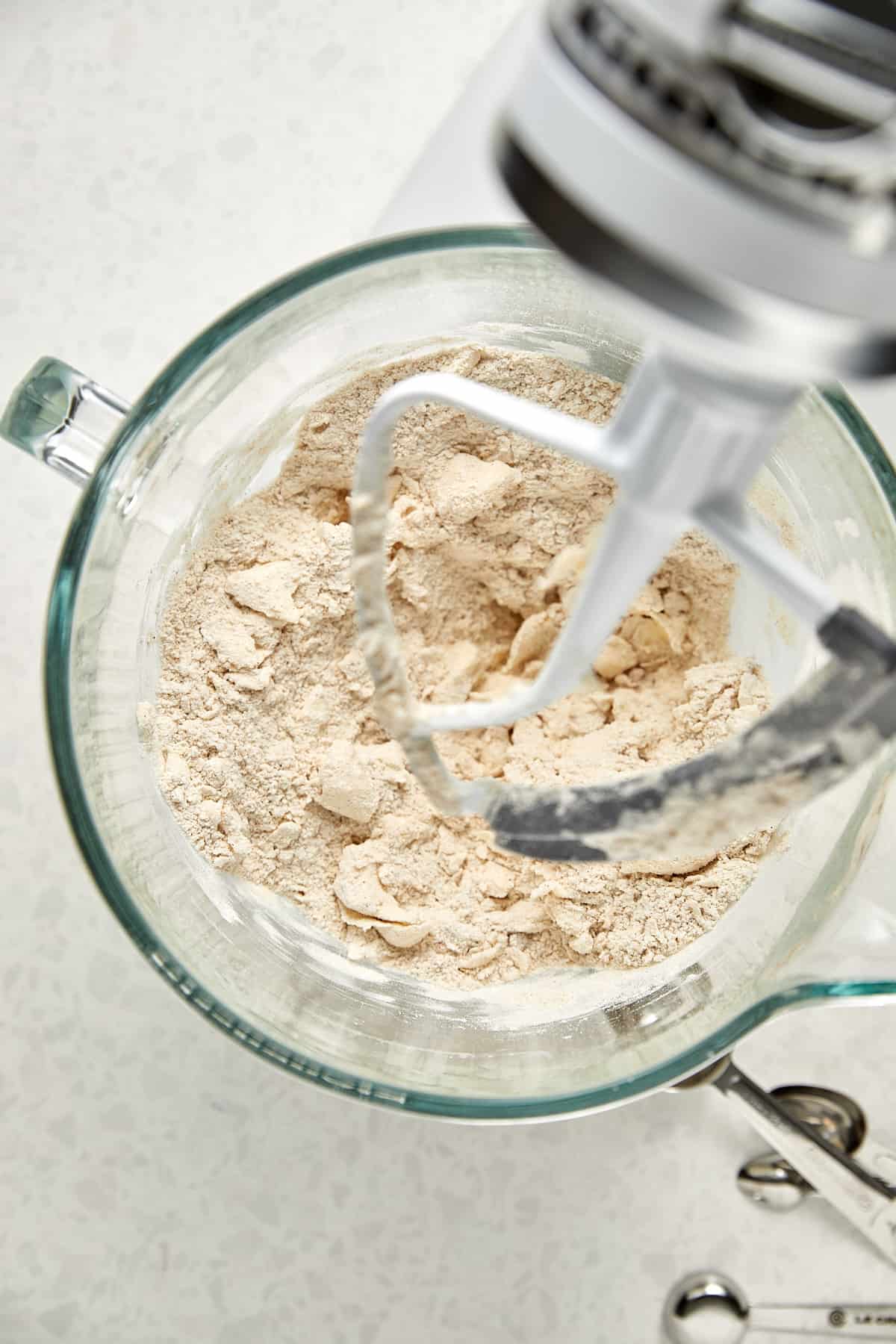 flour and butter in a clear bowl on a kitchen aid mixer after being mixed together. 