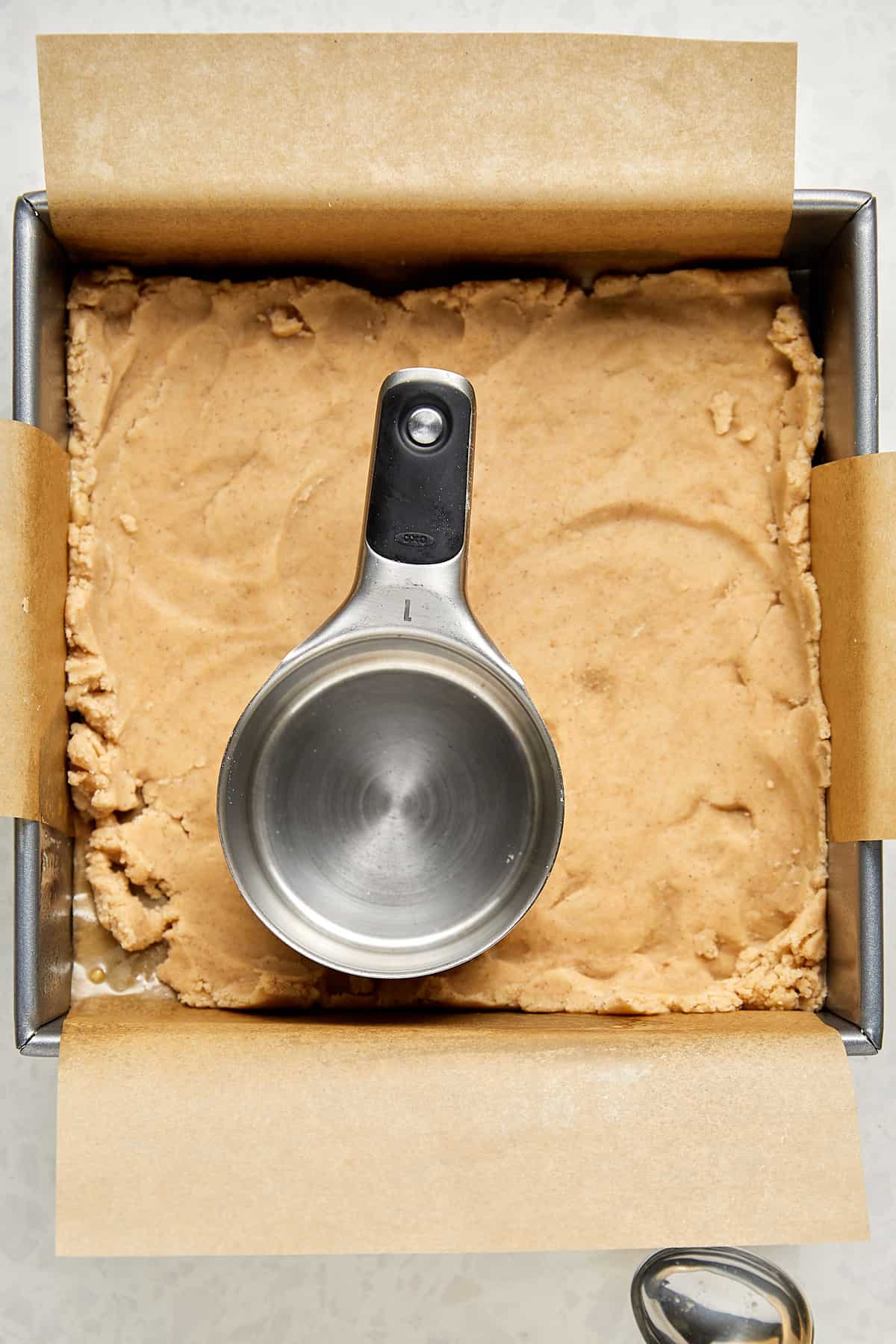 raw dough in an 8x8 metal pan with a measuring cup. 