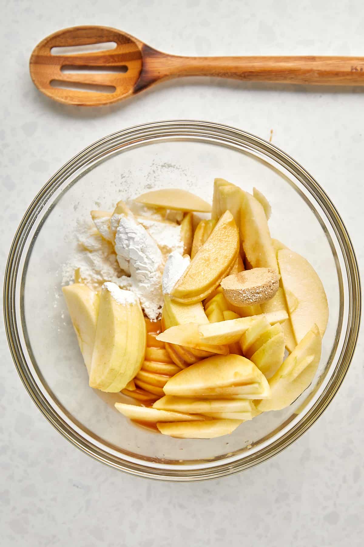 Slices of apples with lemon juice, salted caramel, tapicoa flour, brown sugar, vanilla and salt in a glass bowl.
