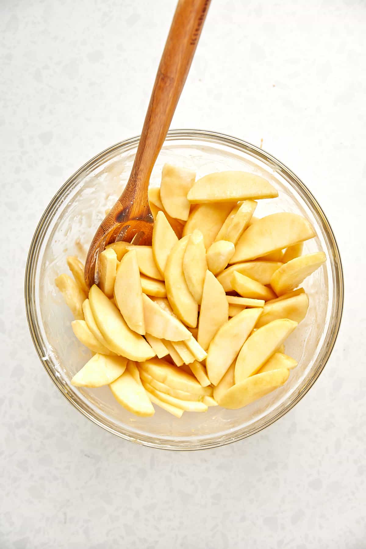 Sliced apples in a clear bowl after mixed with lemon juice, salted caramel, tapicoa flour, sugar, vanilla and salt.