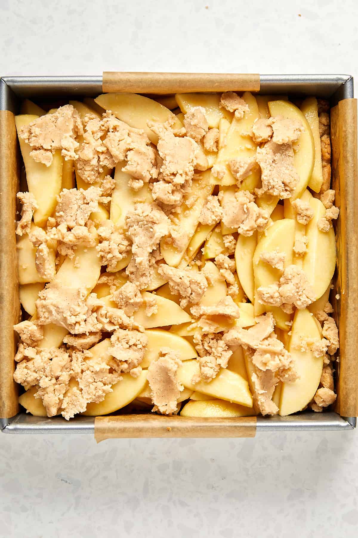 sliced apples on top of cooked dough with raw dough crumbled on top.