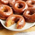 three baked apple cider donuts with apple cider glaze on a white plate with a bite in one donut.
