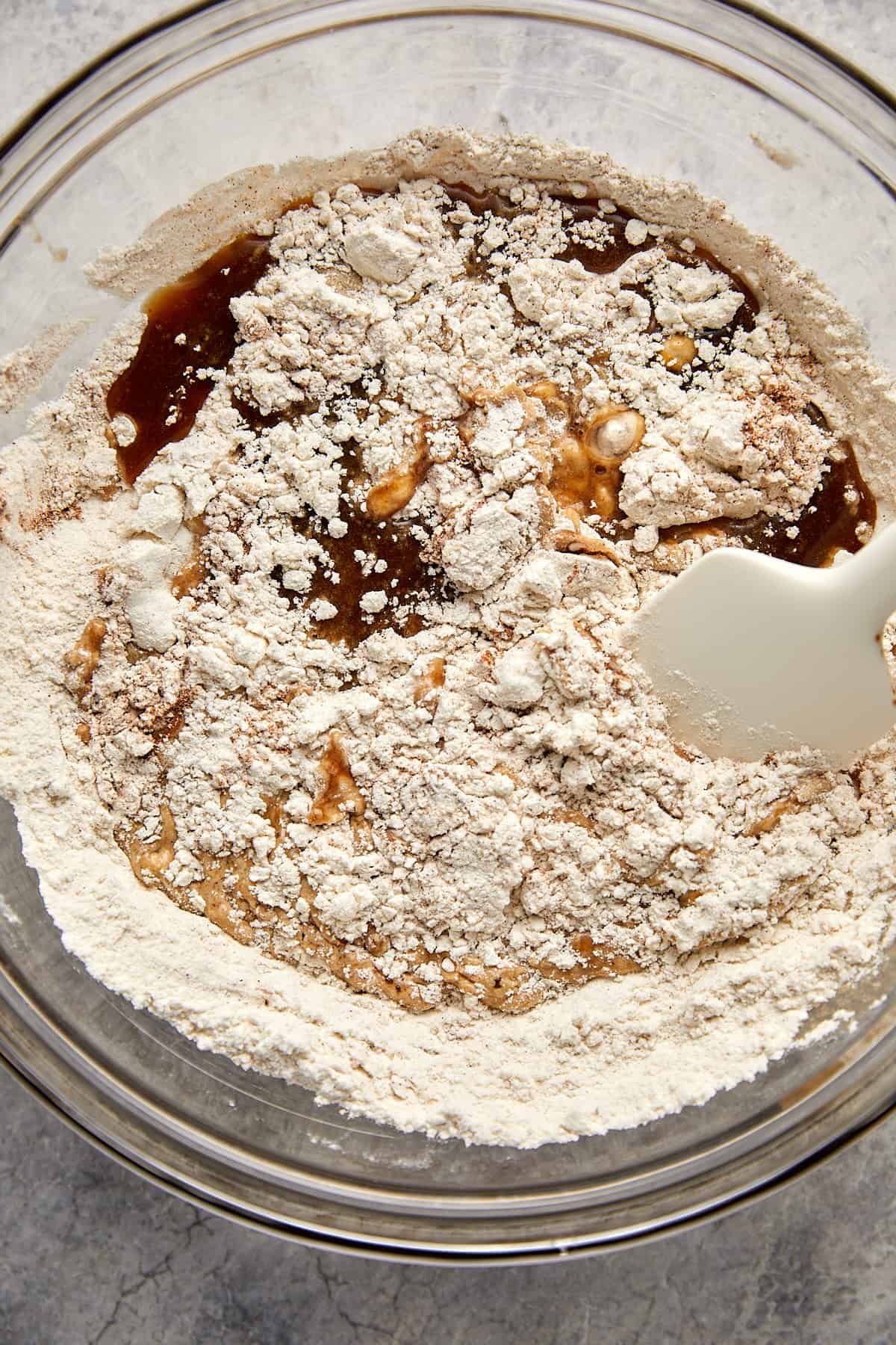 wet ingredients in dry ingredients in a clear bowl with a spatula. 