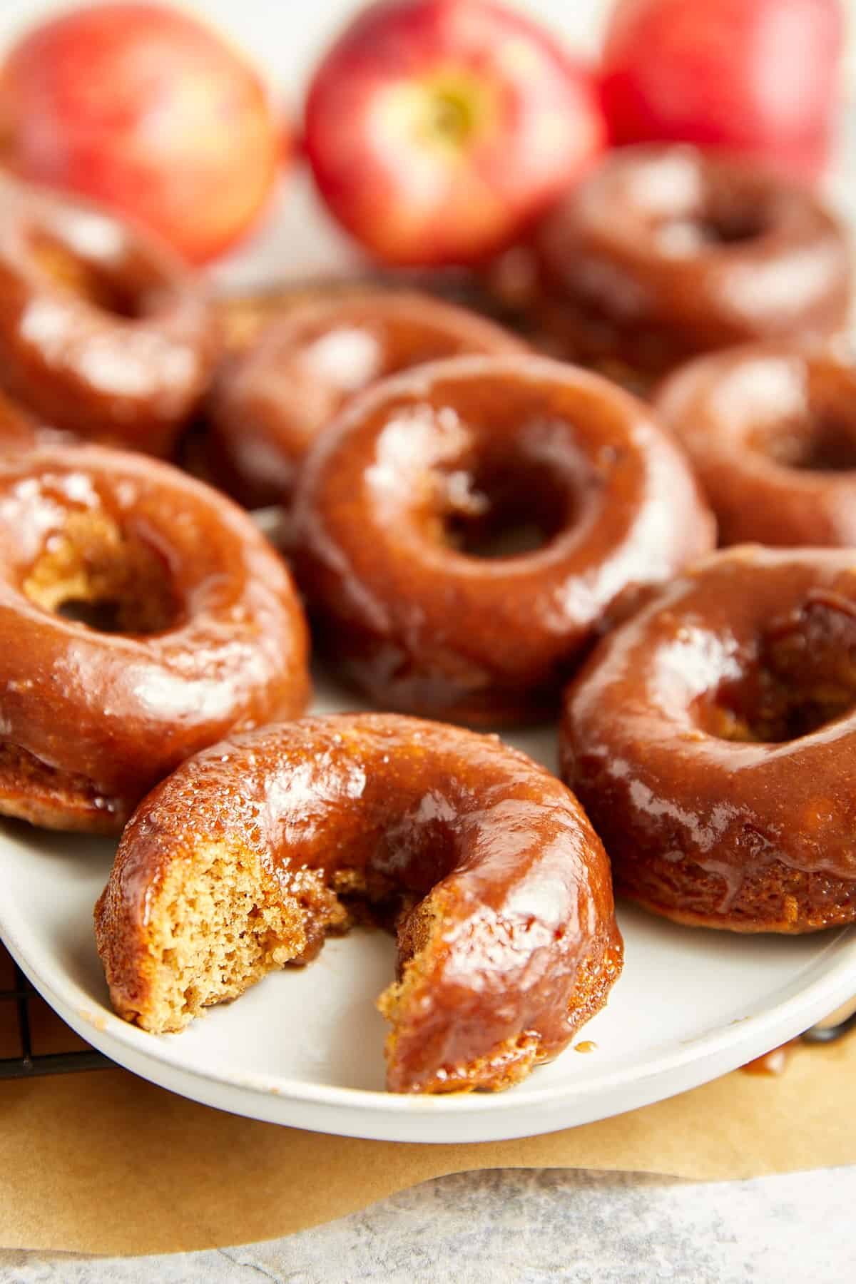 apple cider glazed donuts on a white plate with one bite taken out of one. 