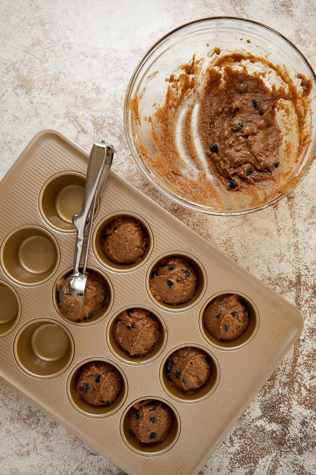 clear bowl with batter scooped out the bowl. muffin tin filled with batter with a cookie scoop.