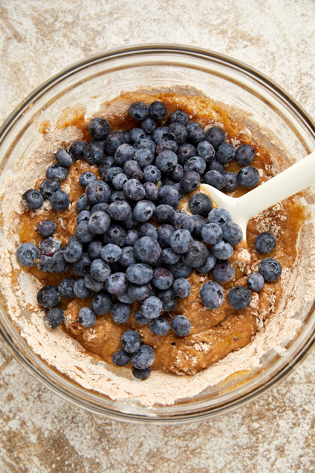 dry and wet ingredients in a clear bowl with blueberries on top.