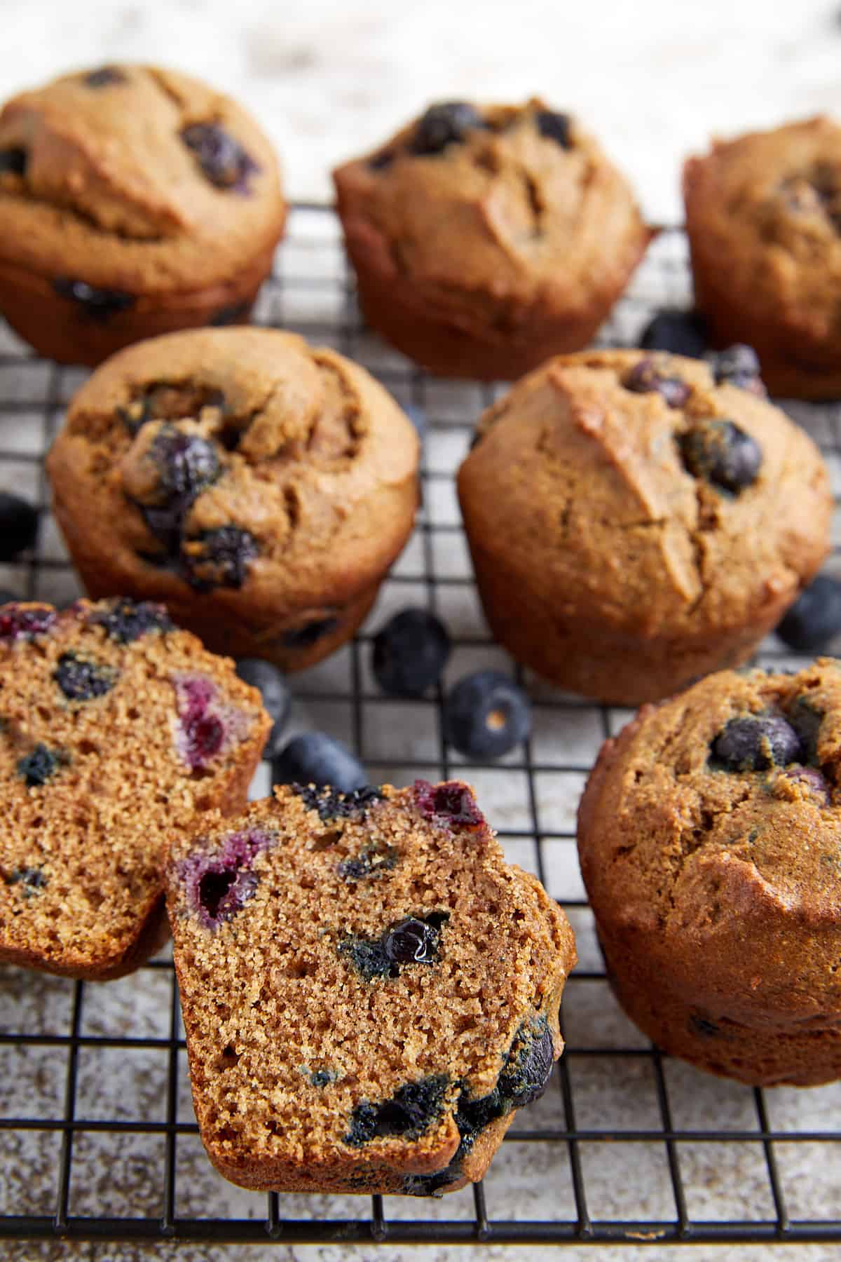 healthy whole wheat blueberry muffins on a cooling rack with blueberries sprinkled throughout.
