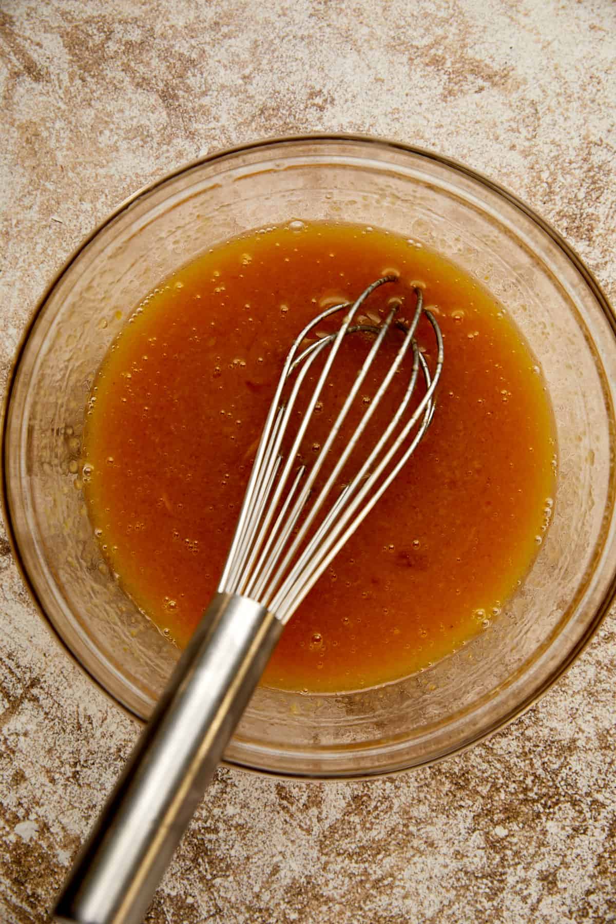 wet ingredients mixed in a clear bowl with a whisk. 