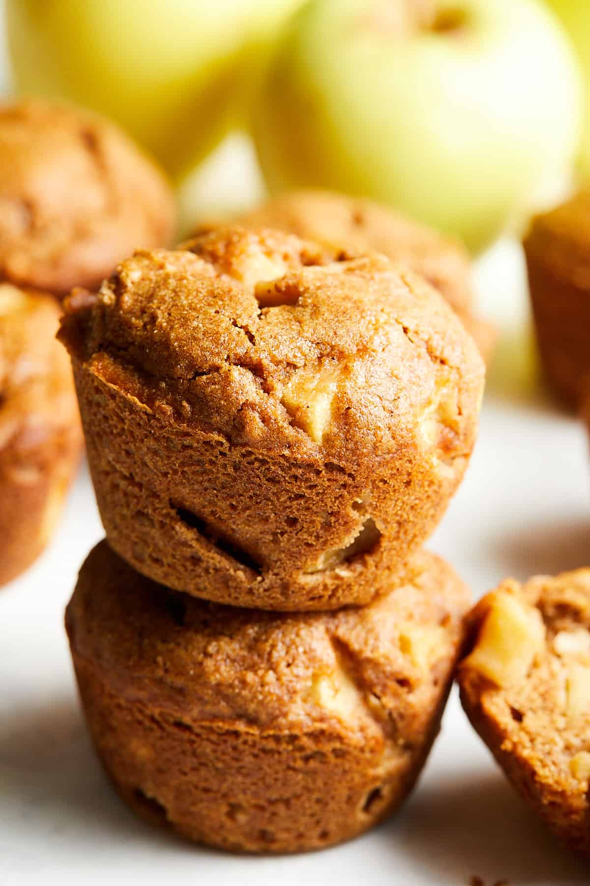 two healthy apple muffins stacked with apples in the background. 
