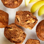 healthy apple muffins spilt in half with whole muffins at the top and sides along with apple slices and one whole apple.