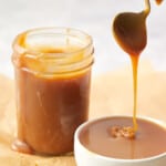 salted caramel drizzling into a white bowl with a full jar of caramel sitting behind bowl.
