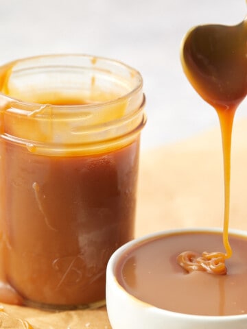 salted caramel drizzling into a white bowl with a full jar of caramel sitting behind bowl.