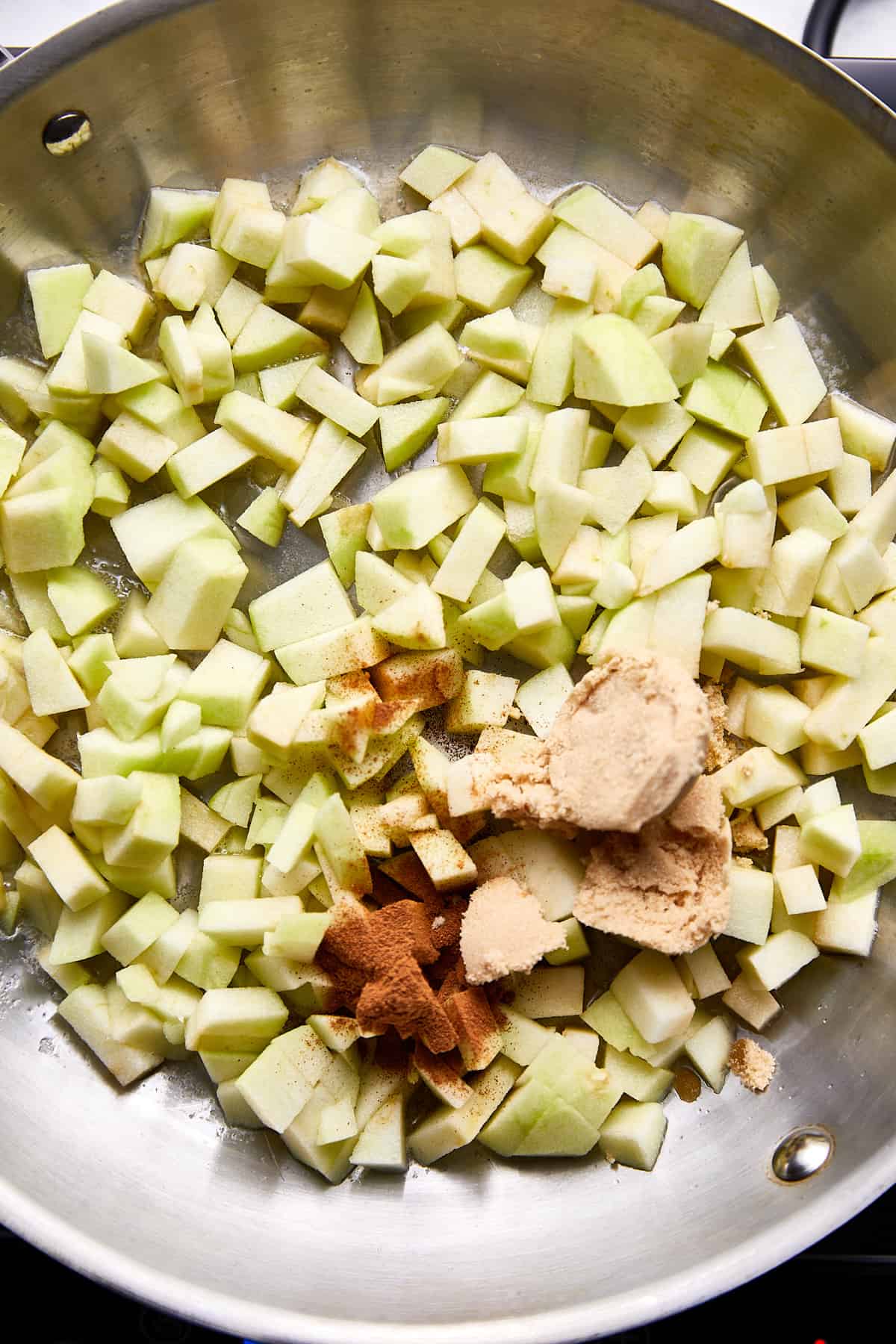 chopped granny smith apples with cinnamon, dark brown sugar, and salt in stainless steel pan. 