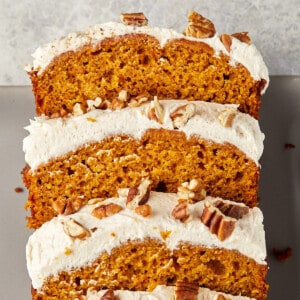 pumpkin bread with cream cheese frosting topped with pecans sliced on a gray plate