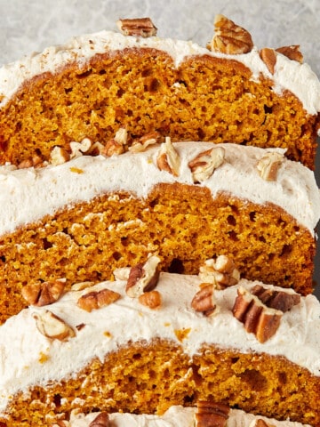 pumpkin bread with cream cheese frosting topped with pecans sliced on a gray plate