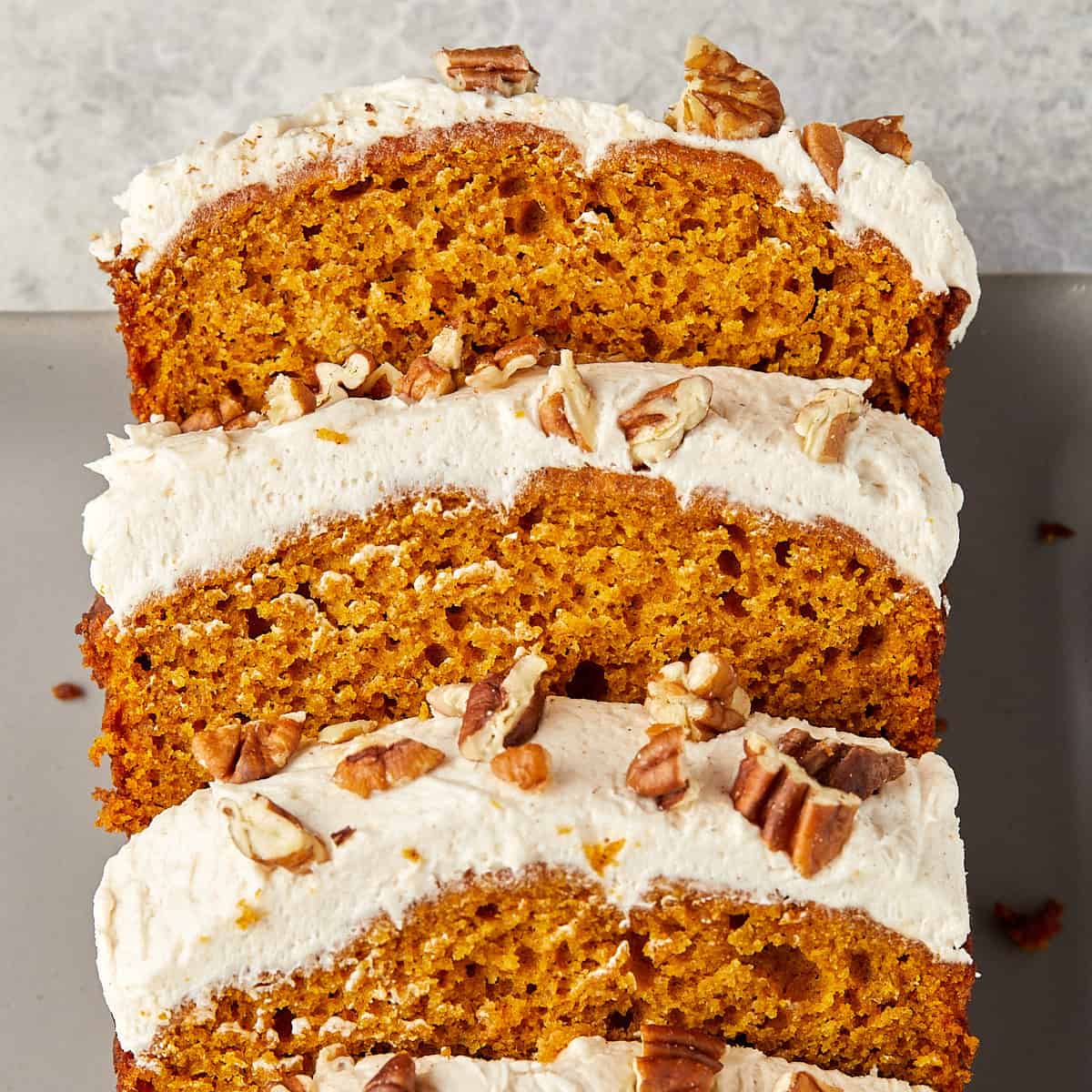 pumpkin bread with cream cheese frosting topped with pecans sliced on a gray plate