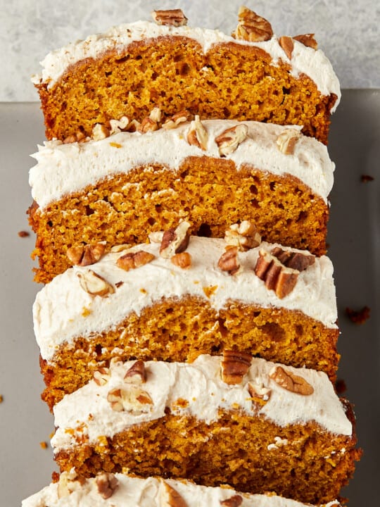 Pumpkin bread with cream cheese topped with toasted pecans sliced on gray plate.