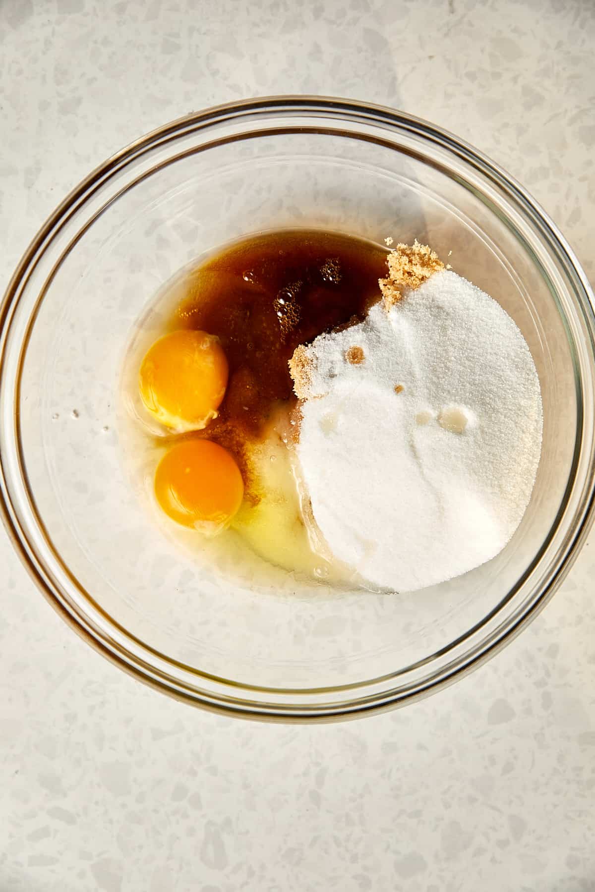 looking down at a glass bowl with eggs, sugar, and vanilla.