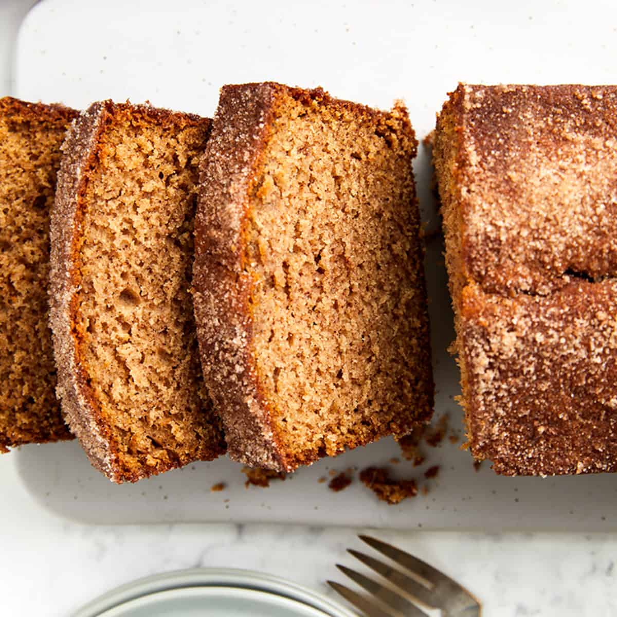 looking down at a bake apple cider loaf bread sliced on a white platter with plates and a fork.