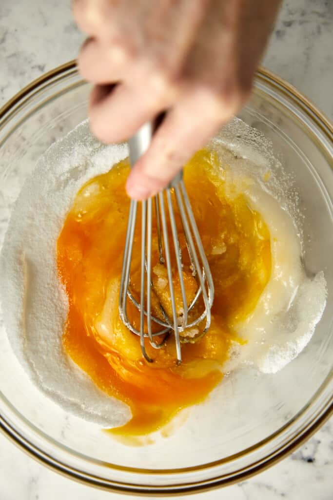 looking down at a glass bowel with eggs and sugar being mixed together.