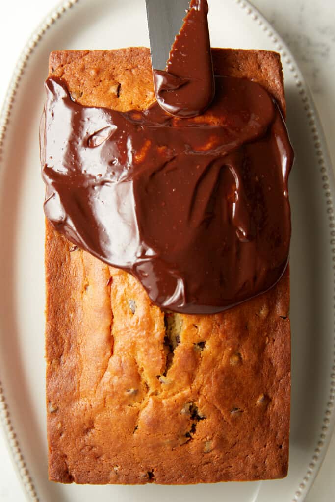chocolate chip loaf cake baked with ganache spread half of the cake with an offset spatula.