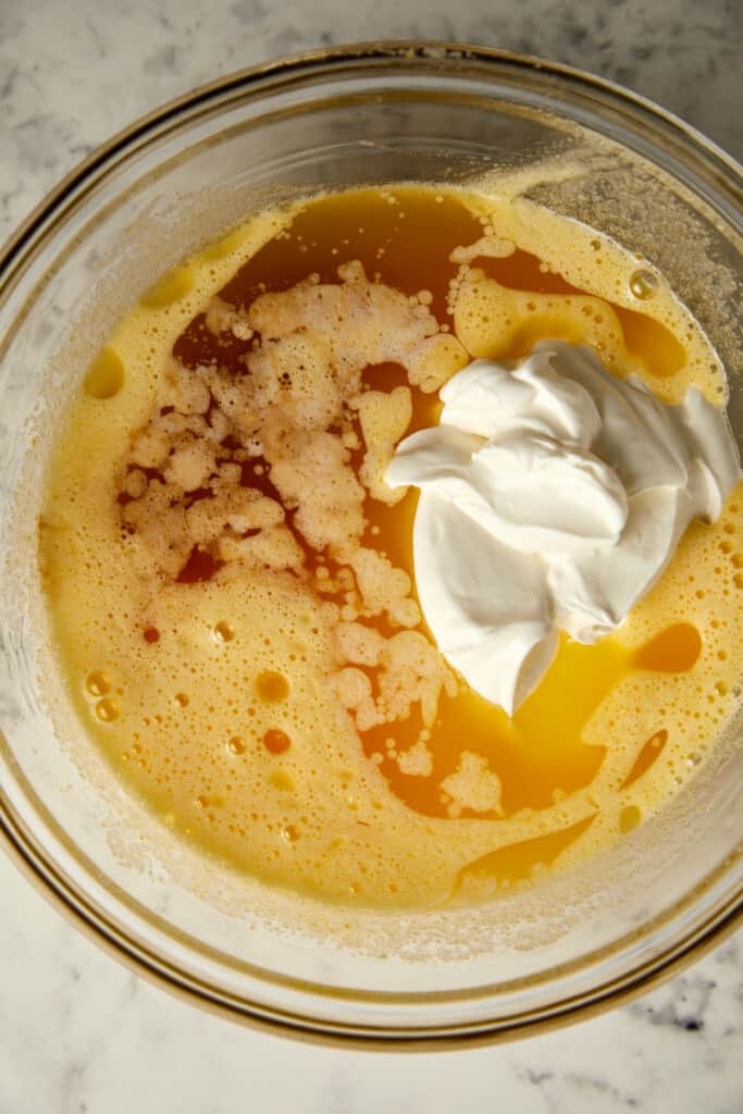 looking down on a glass bowl with vanilla, sour cream, and butter added to eggs and sugar.