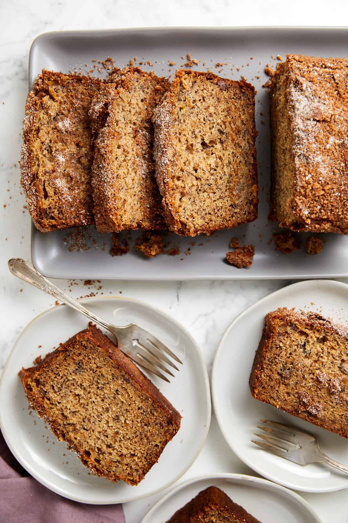 Looking down at cinnamon crunch banana bread sliced on a platter and slices laying on plates with forks.