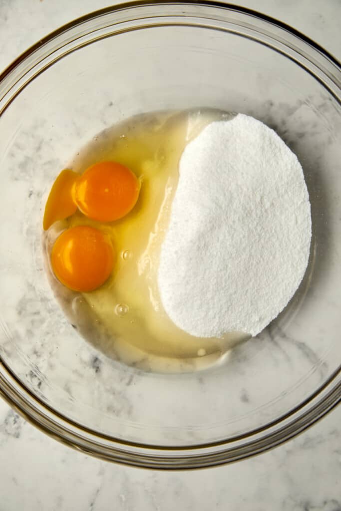 Looking down at eggs and sugar in a glass bowl.