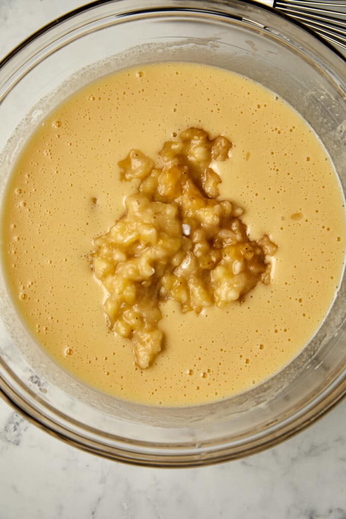 Looking down at glass bowl with wet ingredients with banana laying on top.