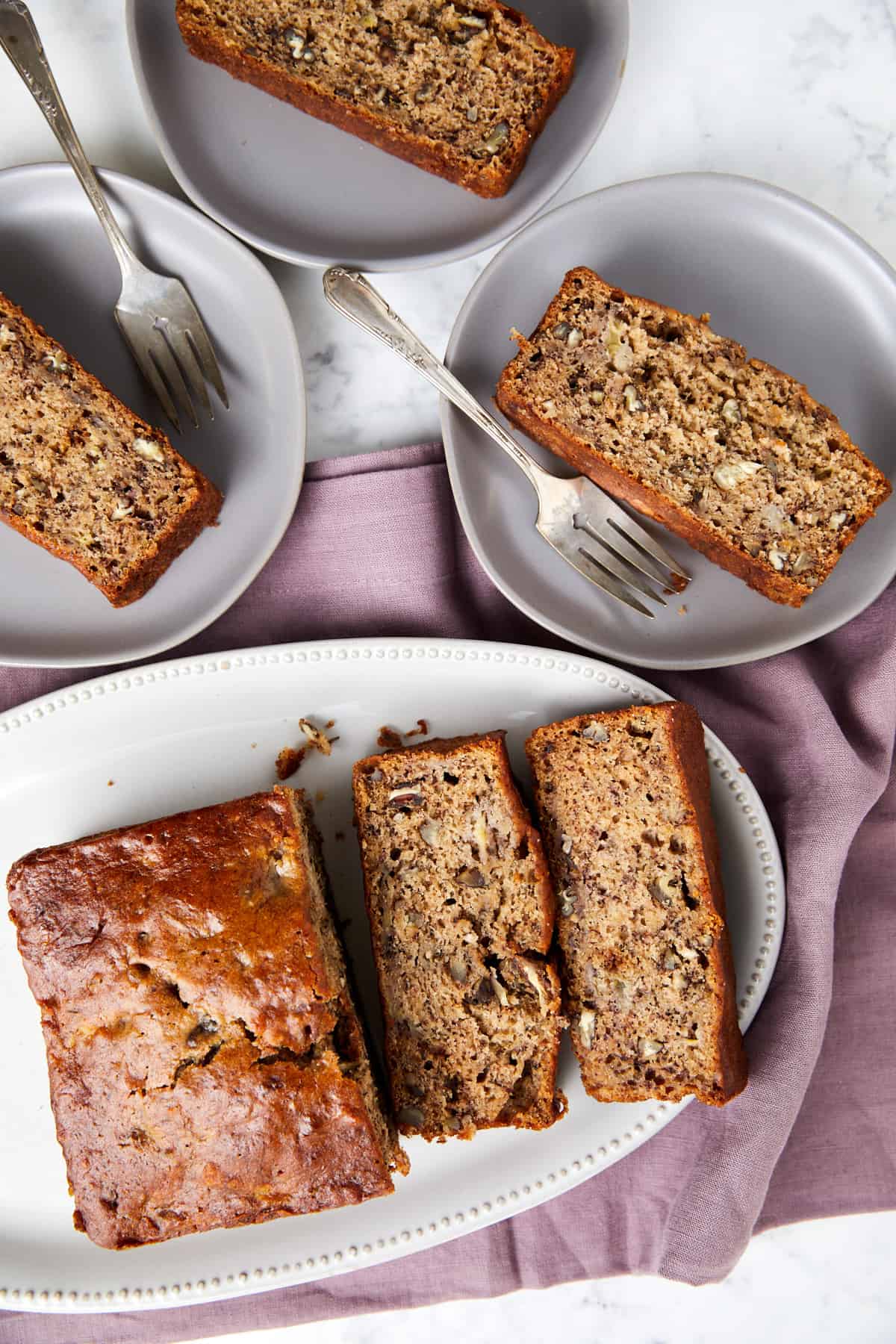 Banana bread with pecans on white platter sliced and slices are are laid on 3 plates with forks.