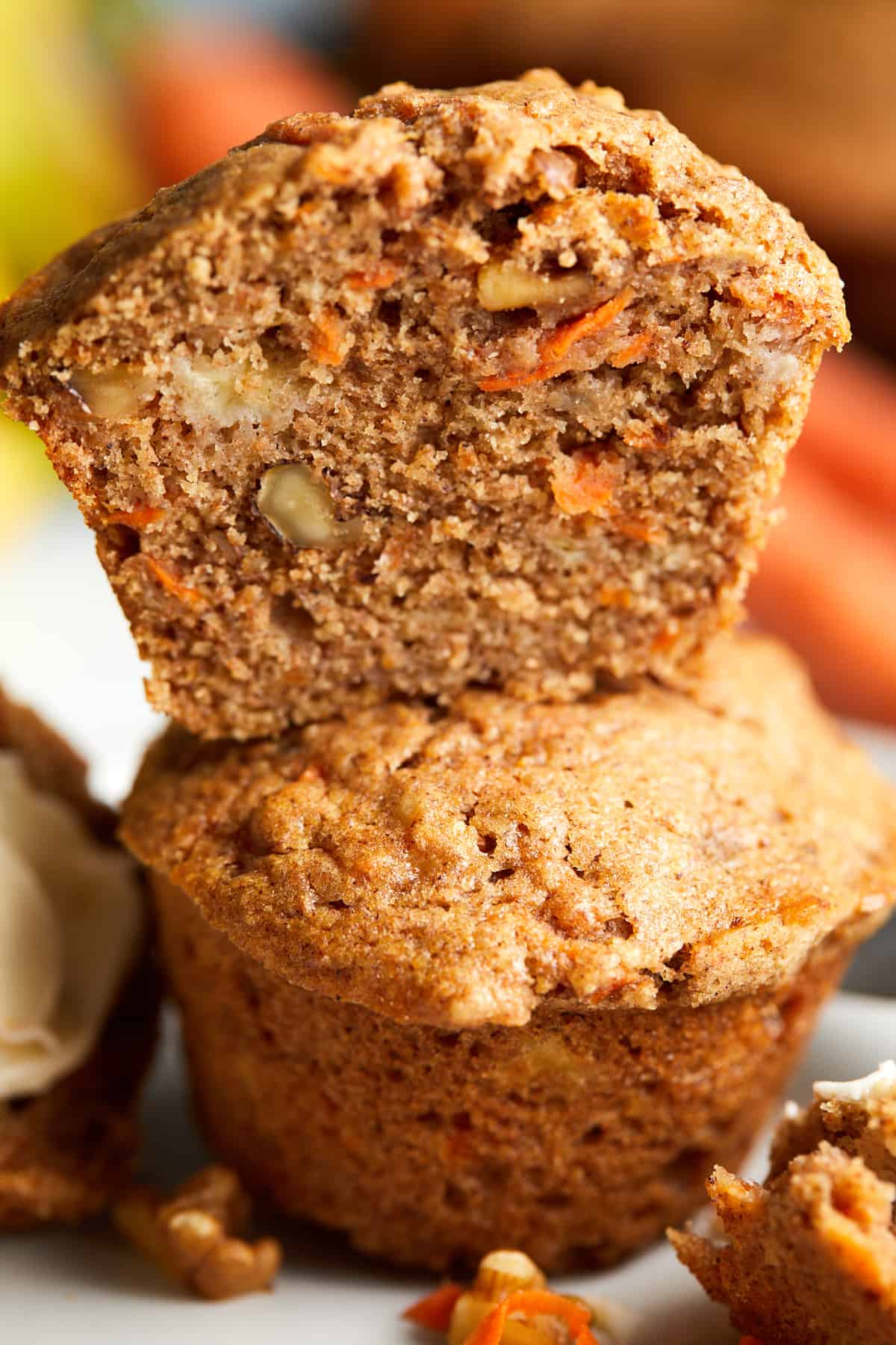 two baked banana carrot muffins sitting on top of each other with the top one sliced in half.