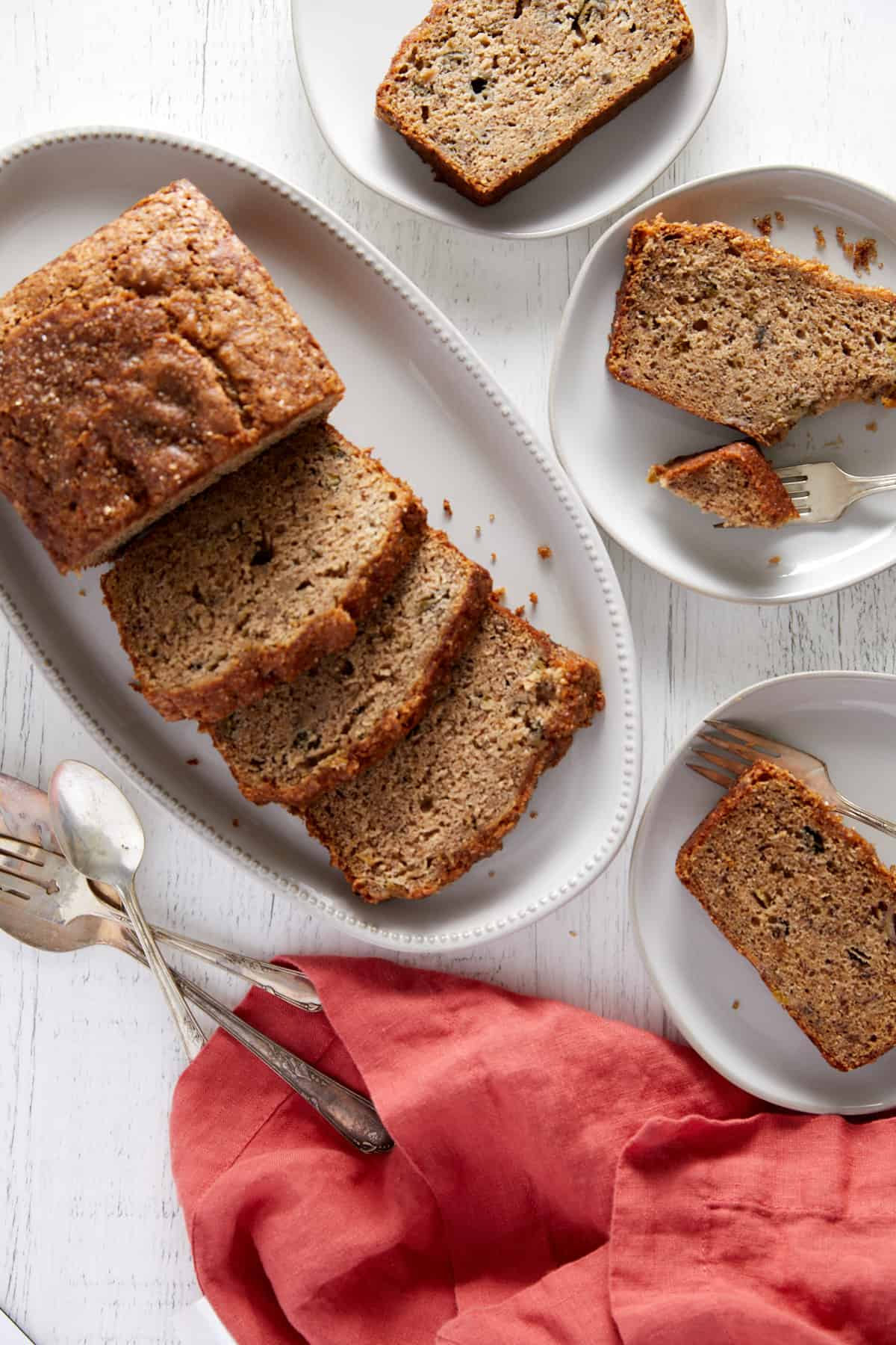 ovehead view of baked rhubarb banana bread on a platter and slices on plates surrounding the platter.